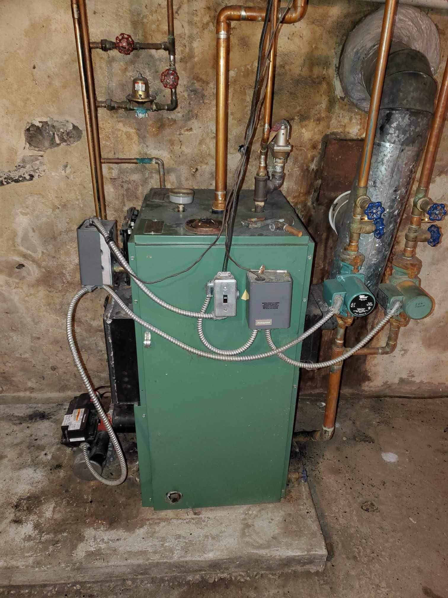A green boiler is sitting in a basement next to copper pipes.