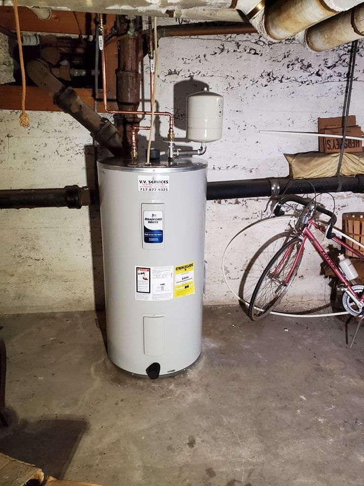 A water heater is sitting in a basement next to a bicycle.