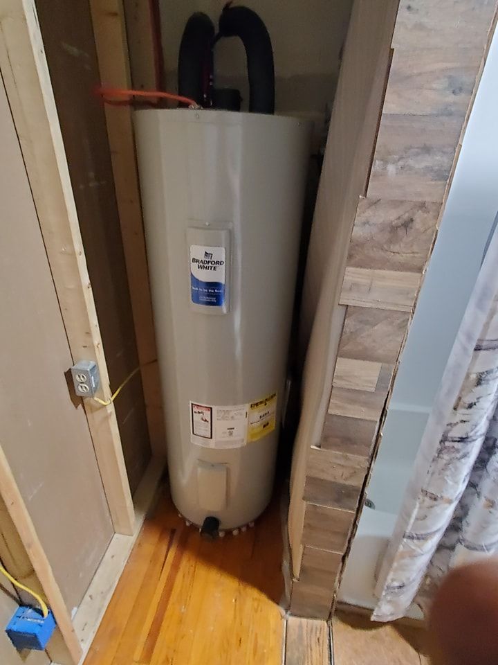 A water heater is sitting in a closet next to a wooden wall.