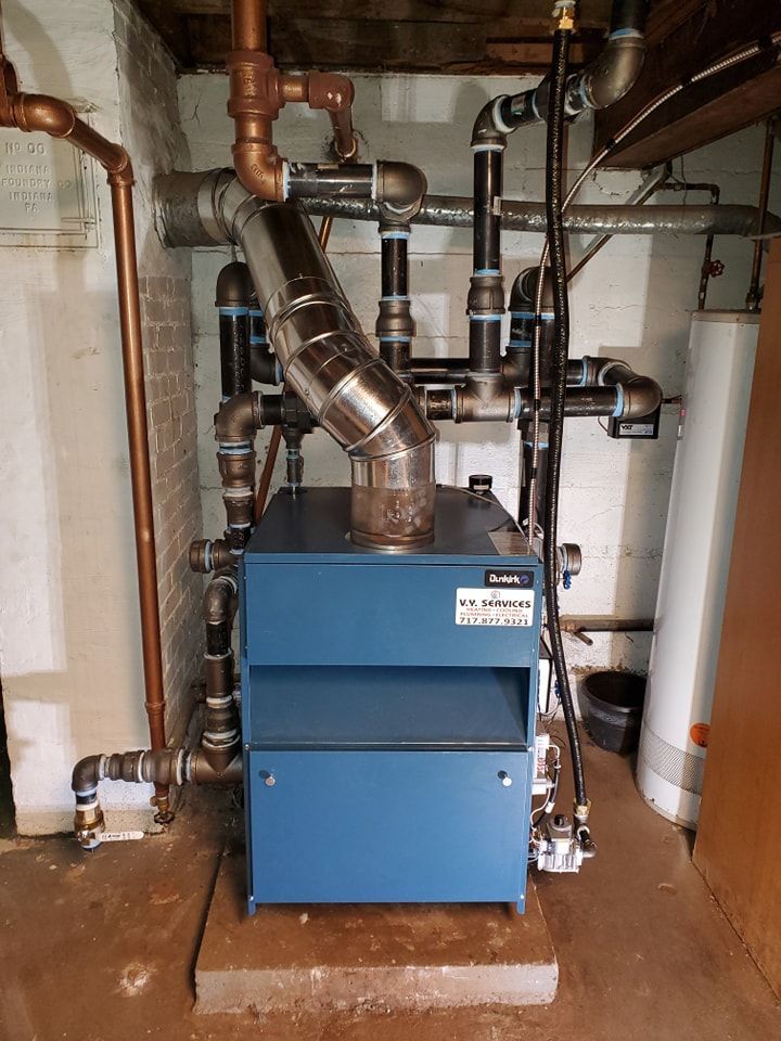 A blue boiler is sitting in a basement surrounded by pipes.