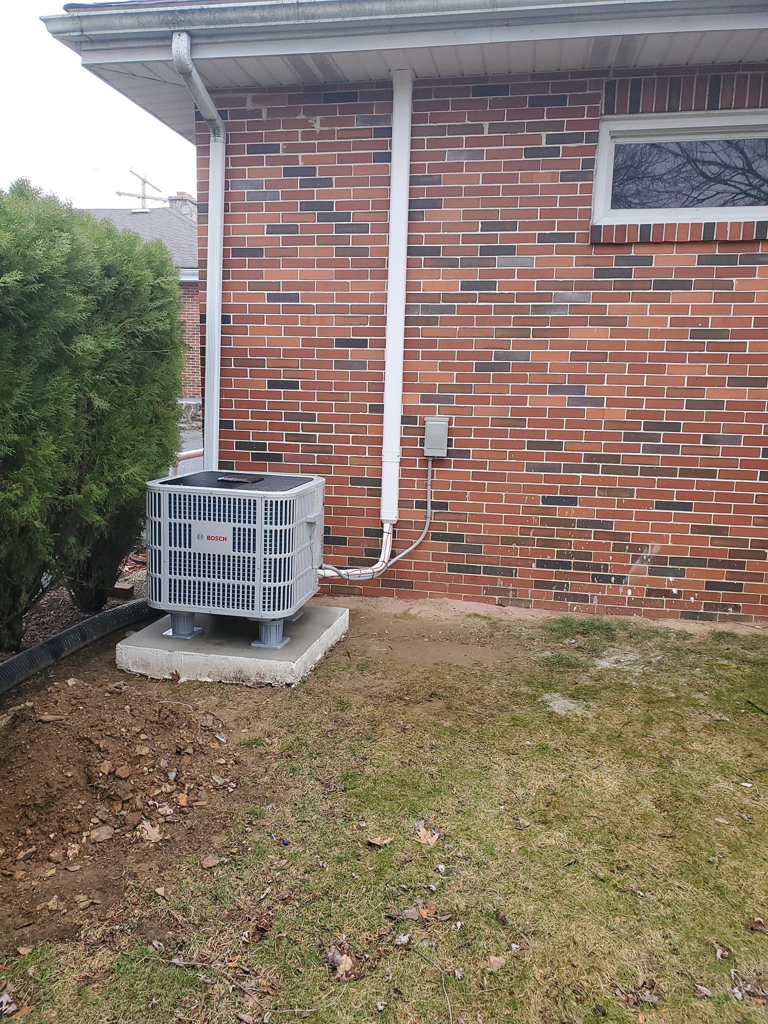 An air conditioner is sitting on the side of a brick house.