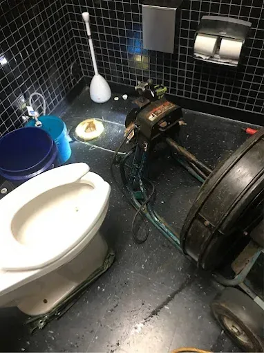Bathroom with toilet, plumbing equipment, and a clogged drain.