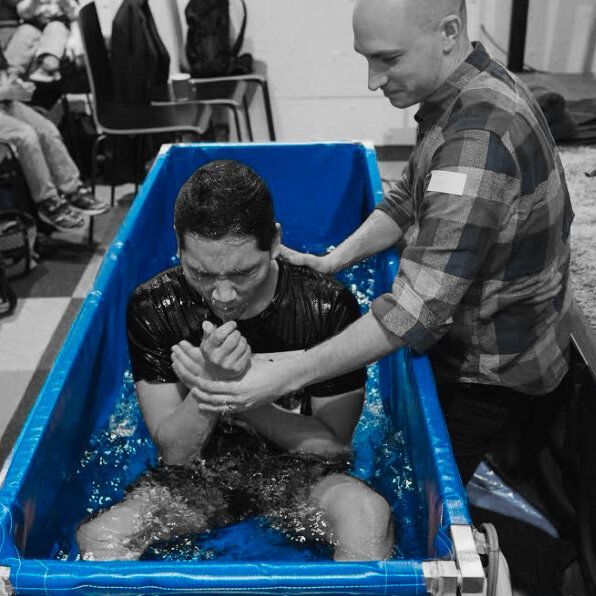 A man is being baptised in a blue tub