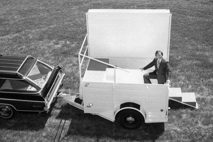 A black and white photo of a man sitting on a trailer