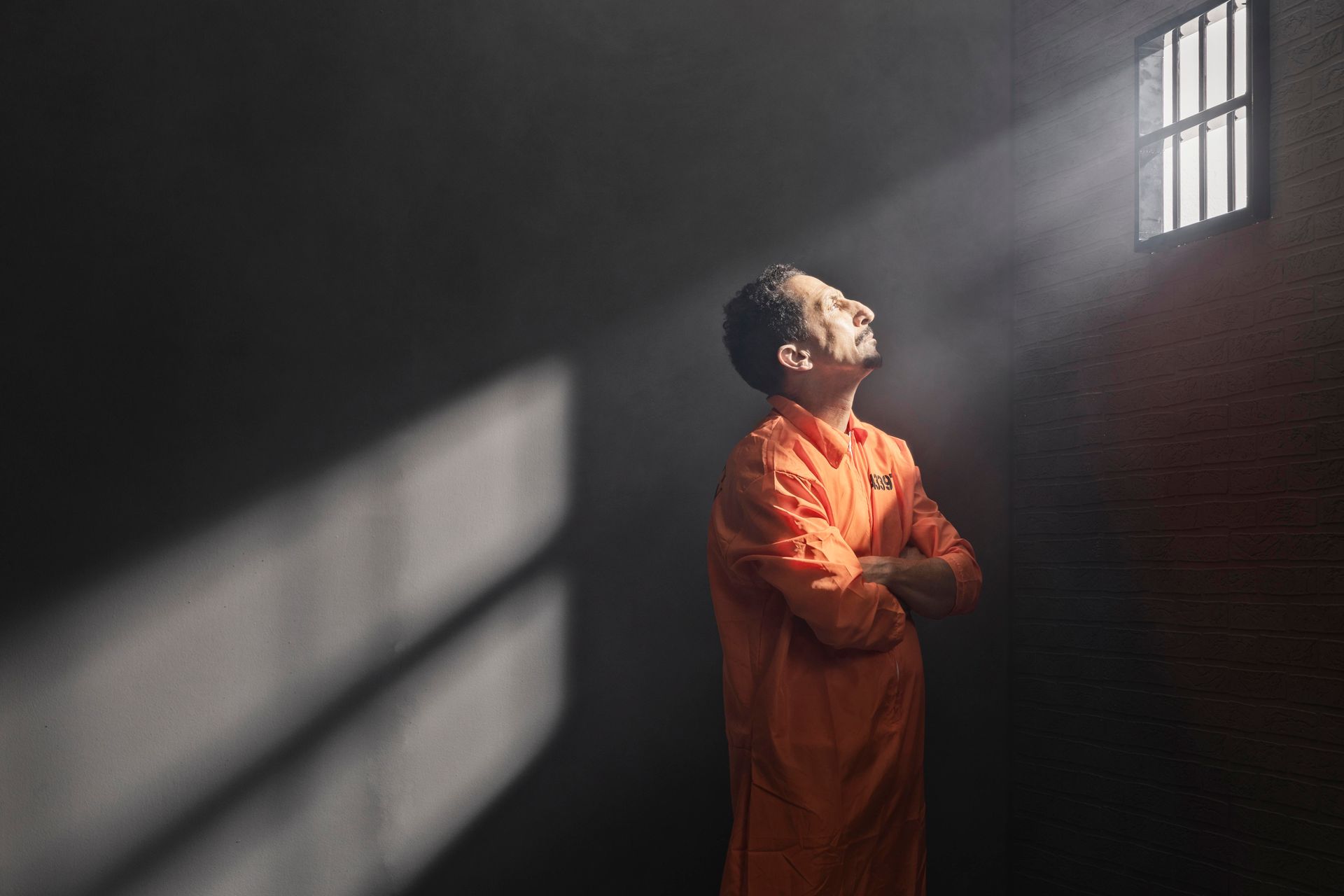 A man in an orange jumpsuit is praying in a prison cell.