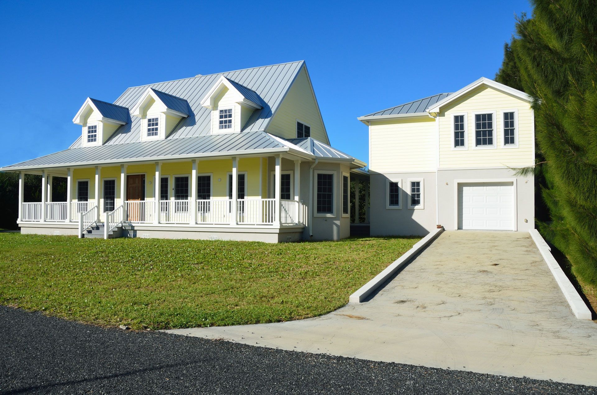 Yellow house with white porch and garage on a green lawn, clear blue sky.