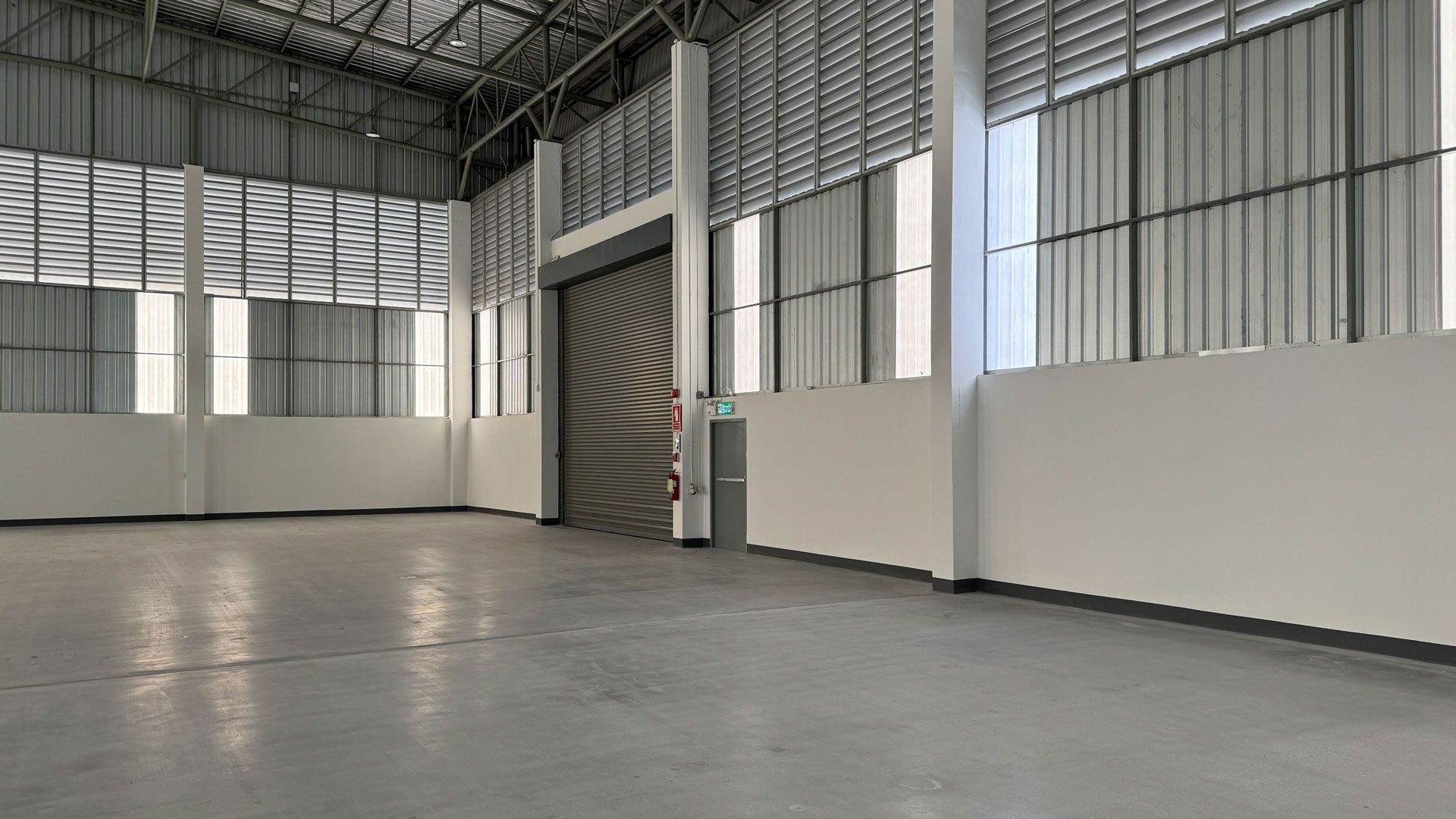 Empty warehouse interior with concrete floor, roll-up door, and metal siding.