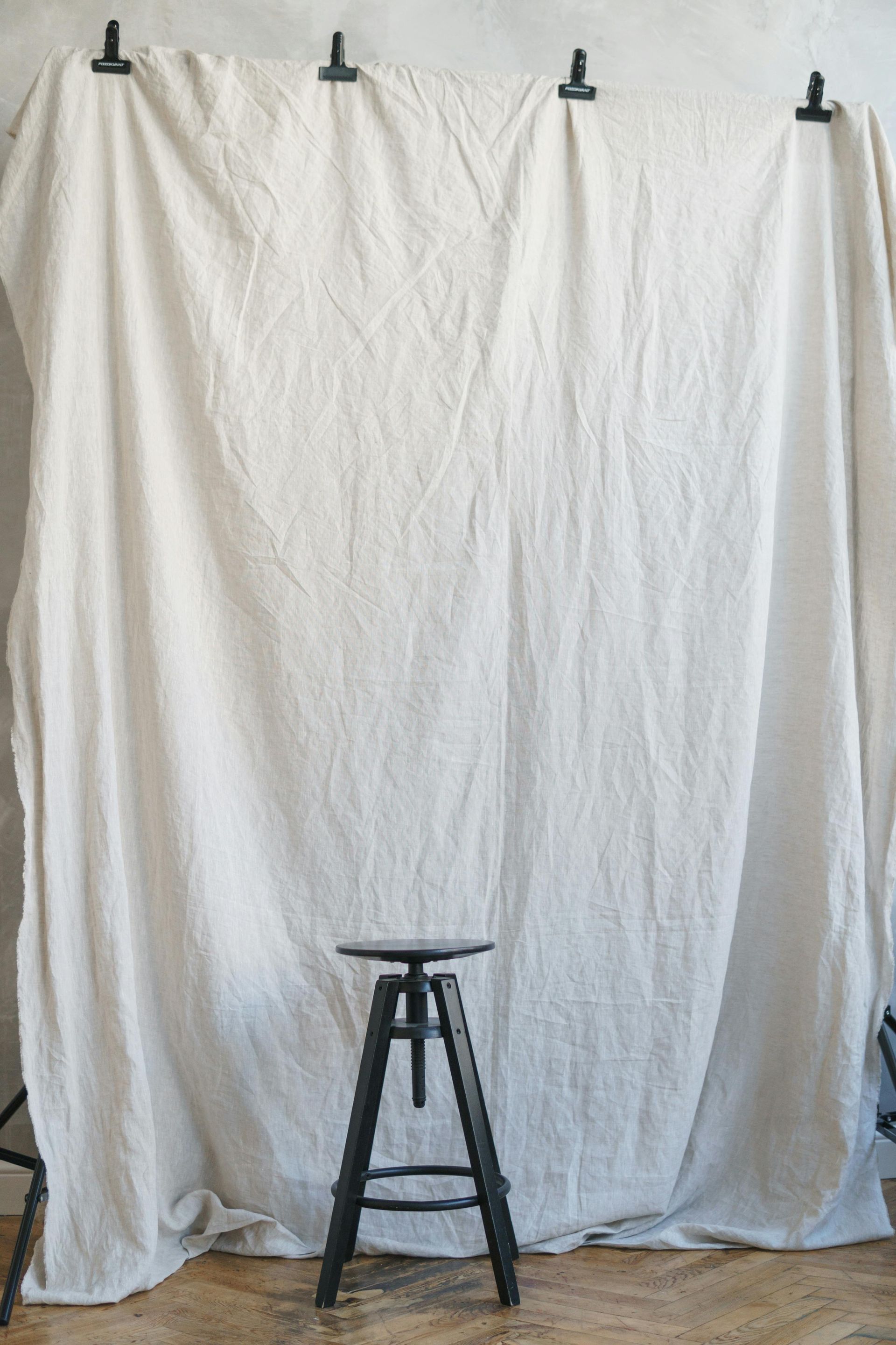 A wooden stool is sitting in front of a white curtain.