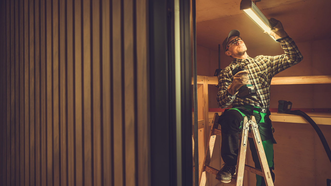 A man is sitting on a ladder holding a light bulb.