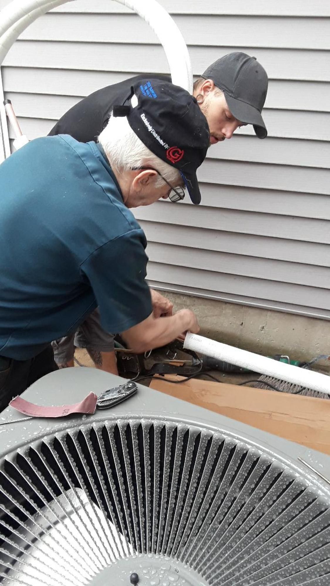 Two men are working on an air conditioner outside of a house.