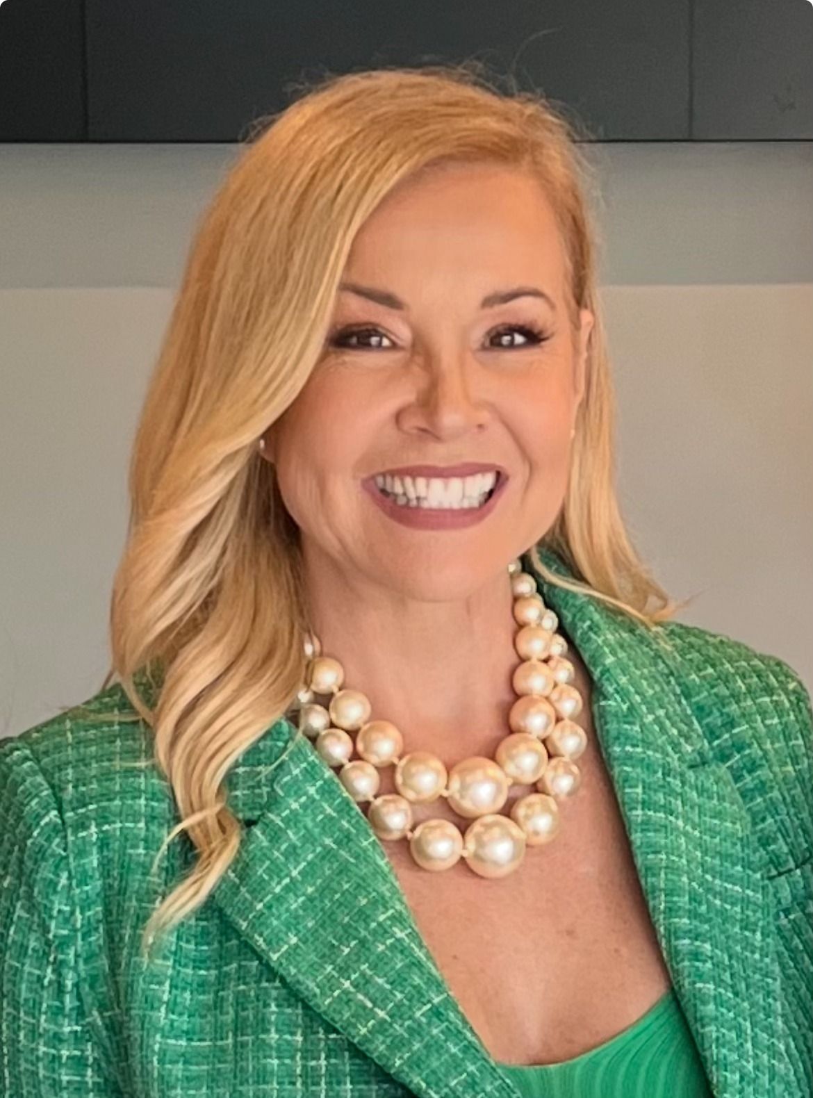 Sandra Peebles is smiling, wearing a green blazer and pearl necklace.