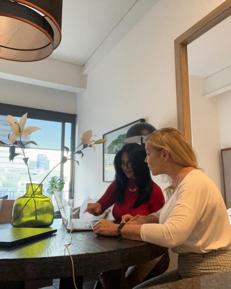 Two women at a table with a laptop, one points at the screen.