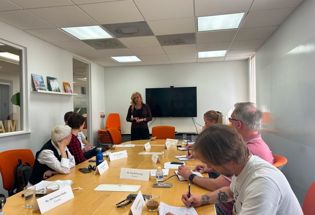 A woman presenting to a group seated around a table in a bright, modern office.