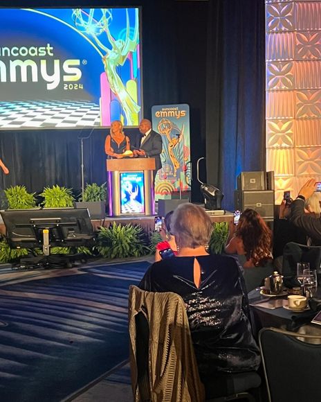 Two people on a stage with a screen, presenting at a formal event, audience seated.