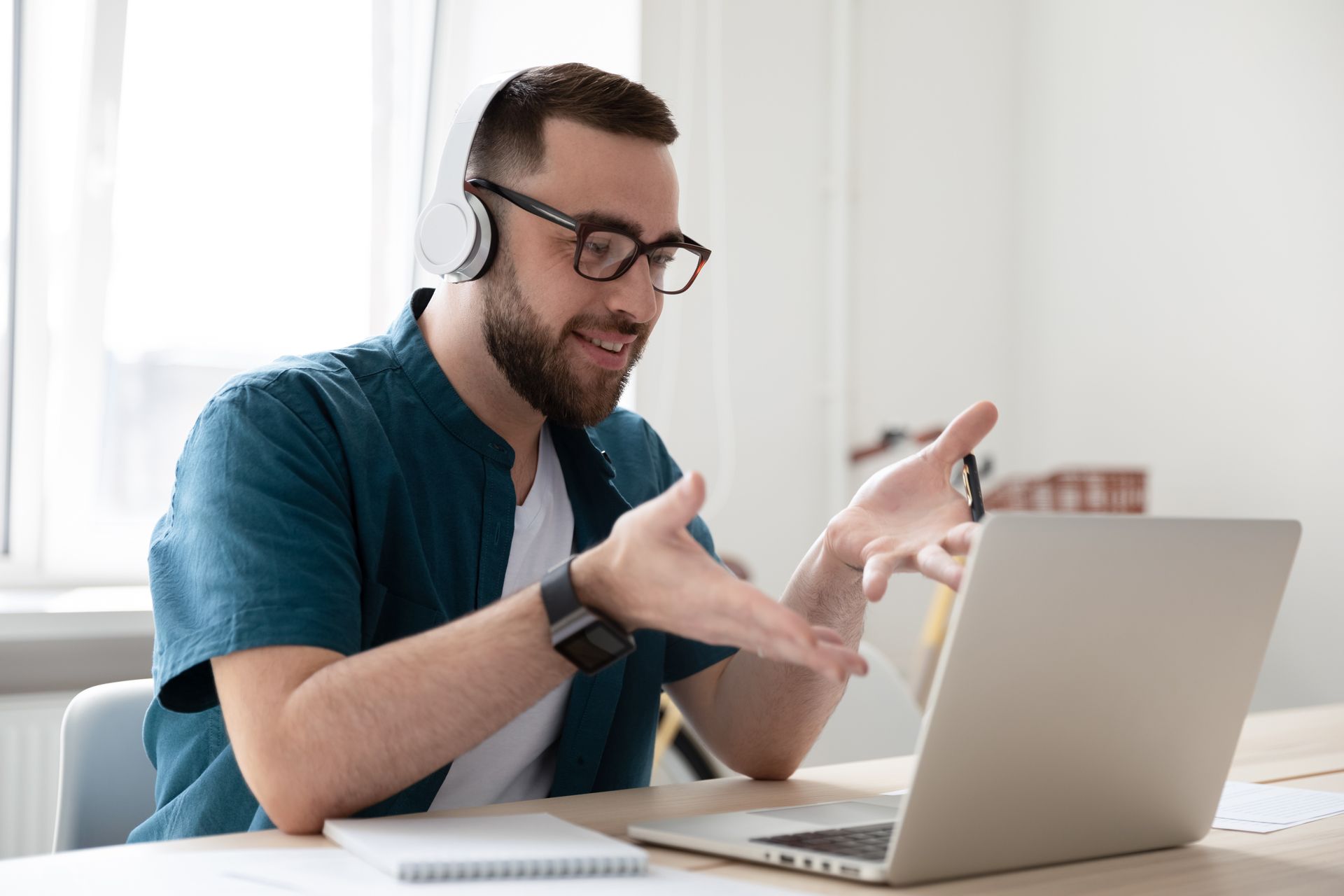 Man wearing headphones and glasses gestures during a video call on a laptop.