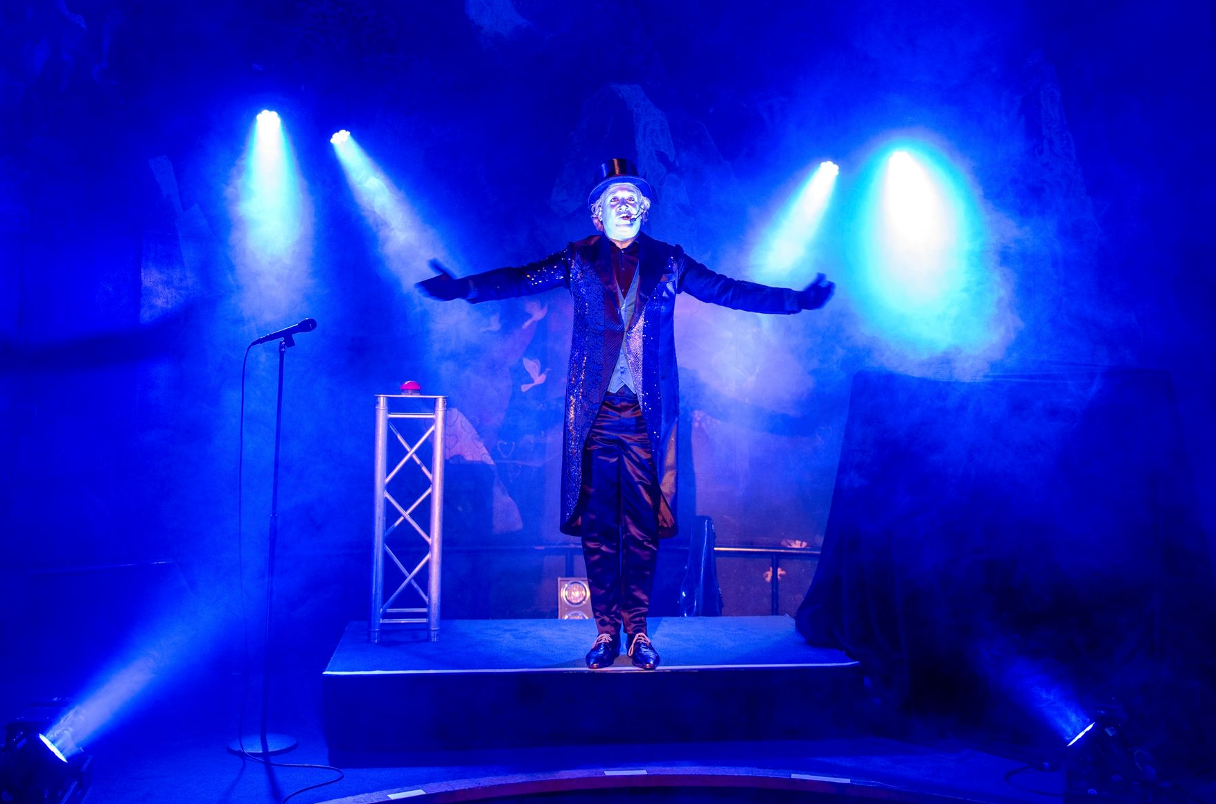 Artiest in kostuum op het podium, armen uitgestrekt, onder blauwe schijnwerpers.