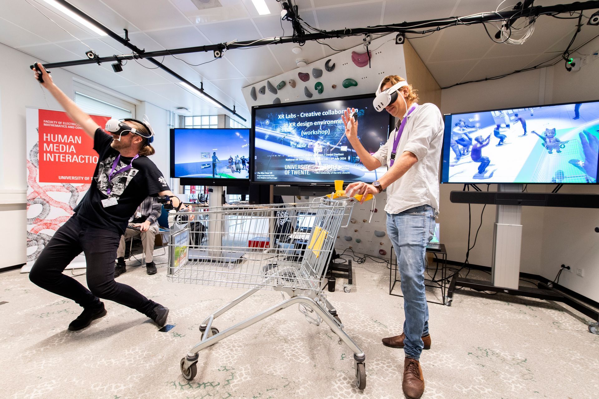 Twee mensen met een VR-bril spelen een spel bij een winkelwagentje in een felverlichte kamer.