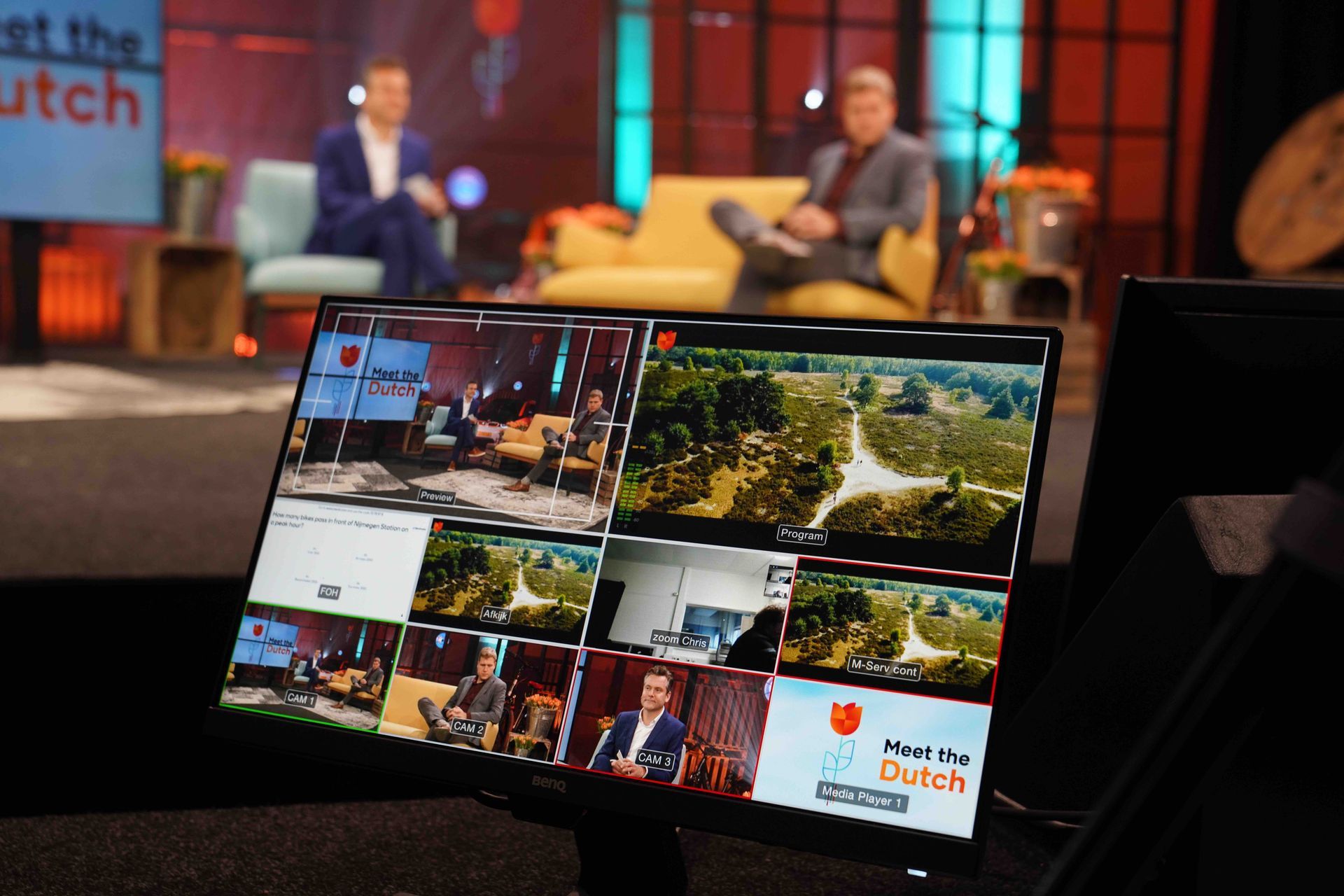 Monitor met meerdere camerabeelden van een televisietoestel met twee mannen in een studio-opstelling.