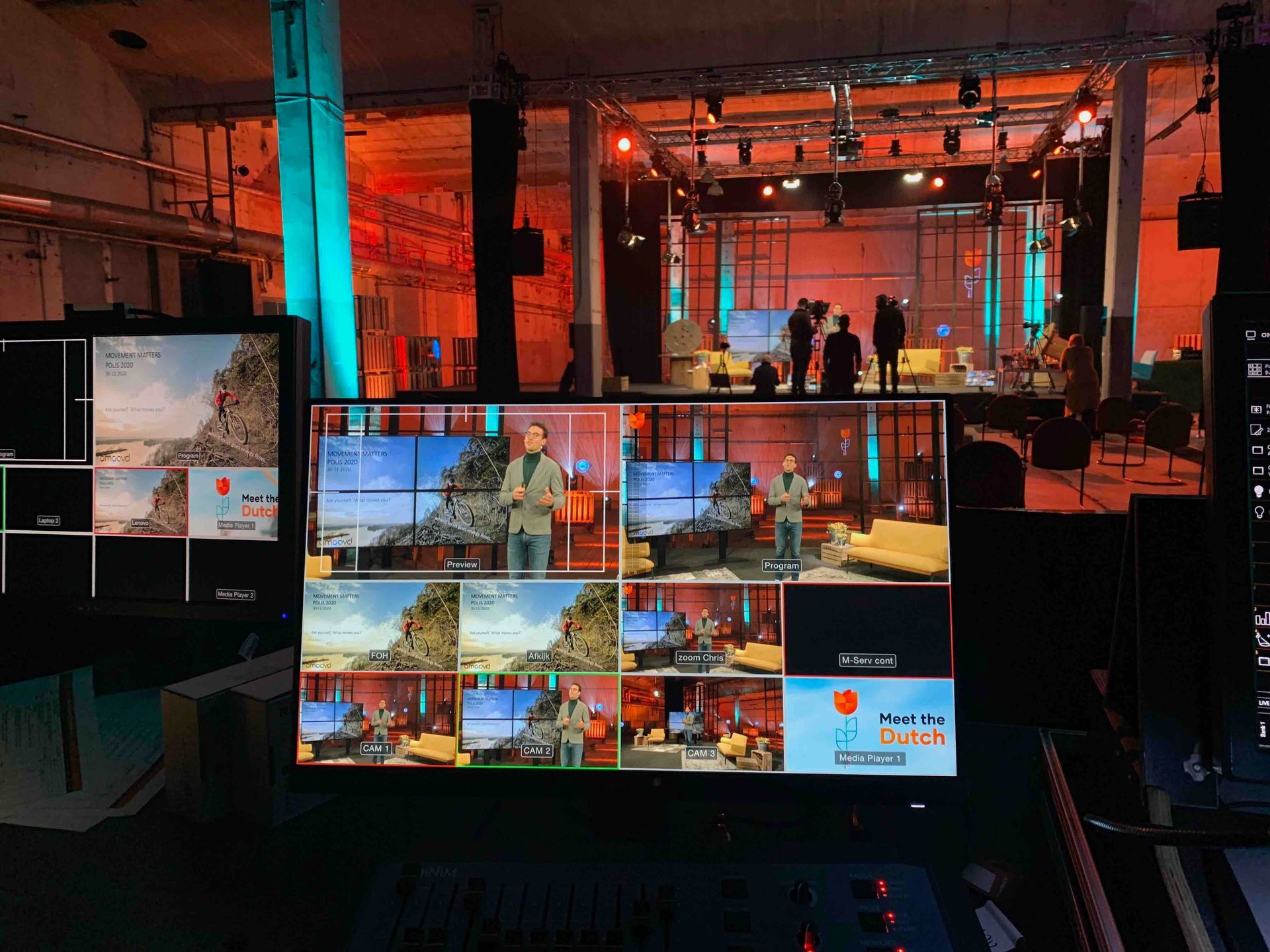 Televisiestudio met monitoren die livebeelden weergeven en met crew op de achtergrond.