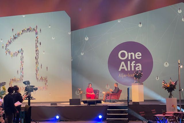 Twee mensen op het podium tijdens een evenement met het logo van