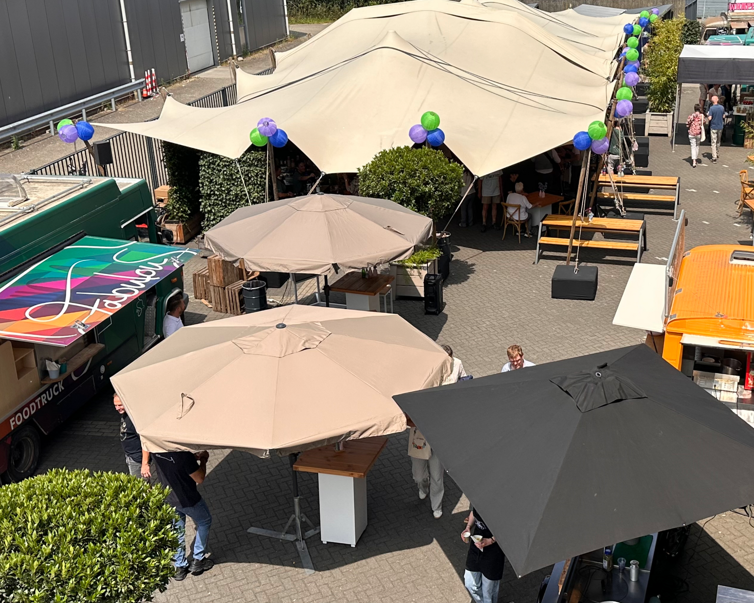 Buitenvoedselmarkt met tenten, parasols, foodtrucks en mensen.