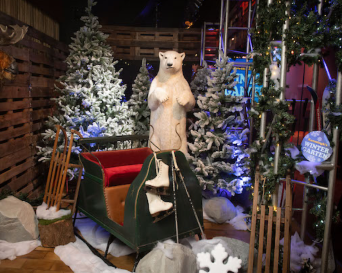 Wintertafereel met een ijsbeerbeeld, slee, besneeuwde bomen en schaatsen.