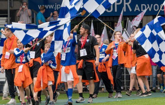 Mensen met blauw-wit geblokte vlaggen en oranje kleding lopen over een veld.