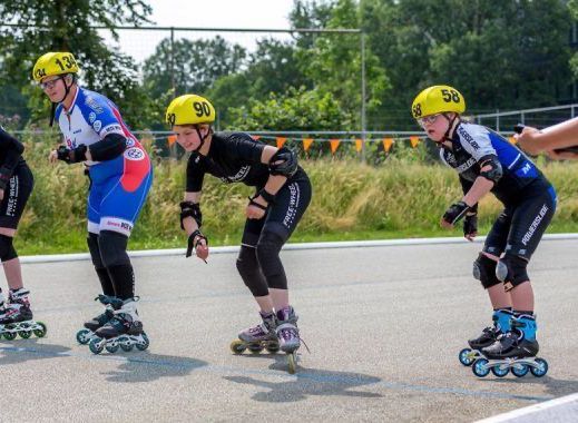 Inline-skaters in startpositie, met helm en beschermende kleding op een verharde baan.