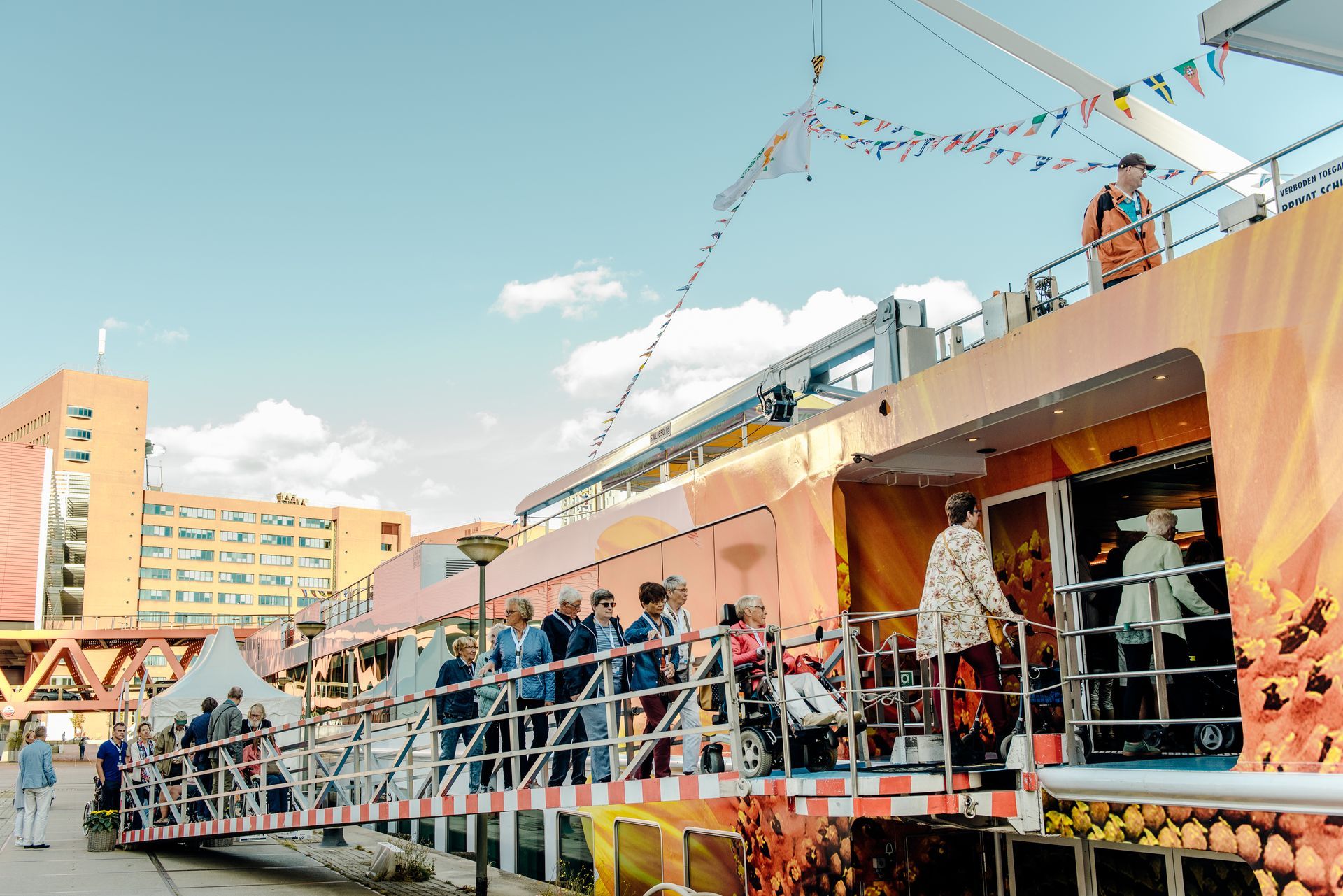 Mensen op een vrolijk versierde pier met een kleurrijk gebouw op de achtergrond.