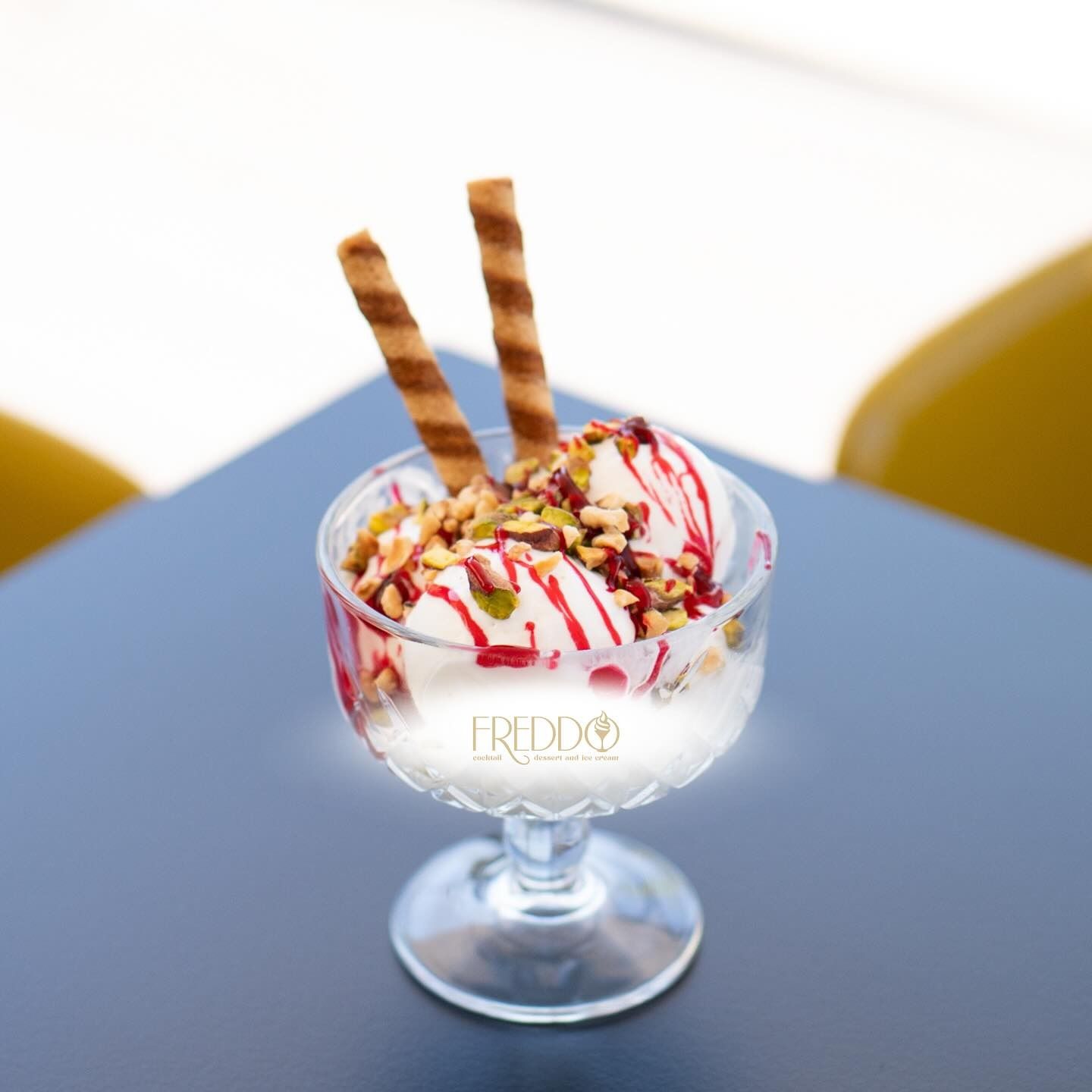 Decorazione murale con fiori colorati e strutturati disposti in file, che ricordano la bandiera italiana. Sedie azzurre e un tavolo di fronte.