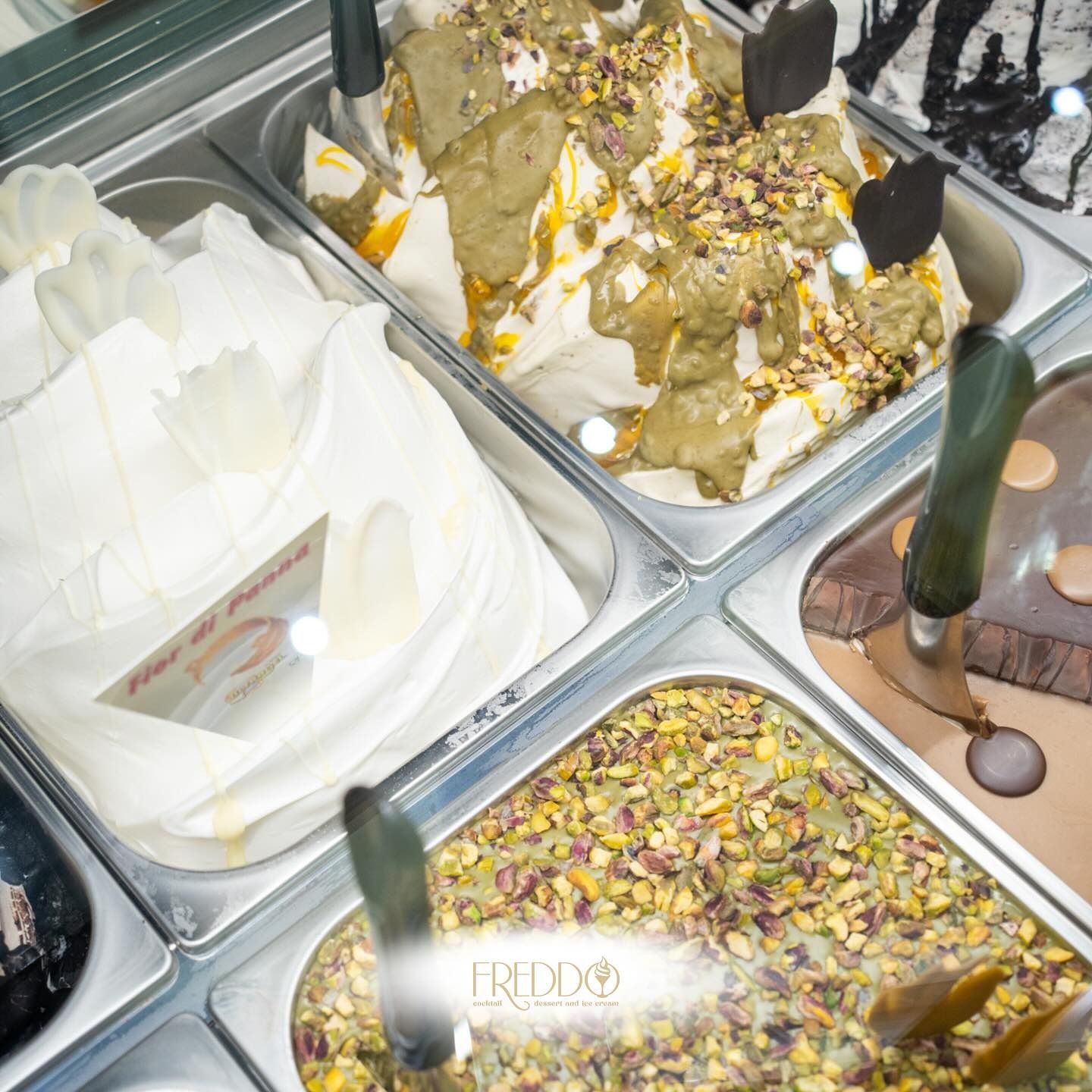 Gelato al pistacchio in un contenitore di metallo con cono e pistacchi su una superficie gialla.