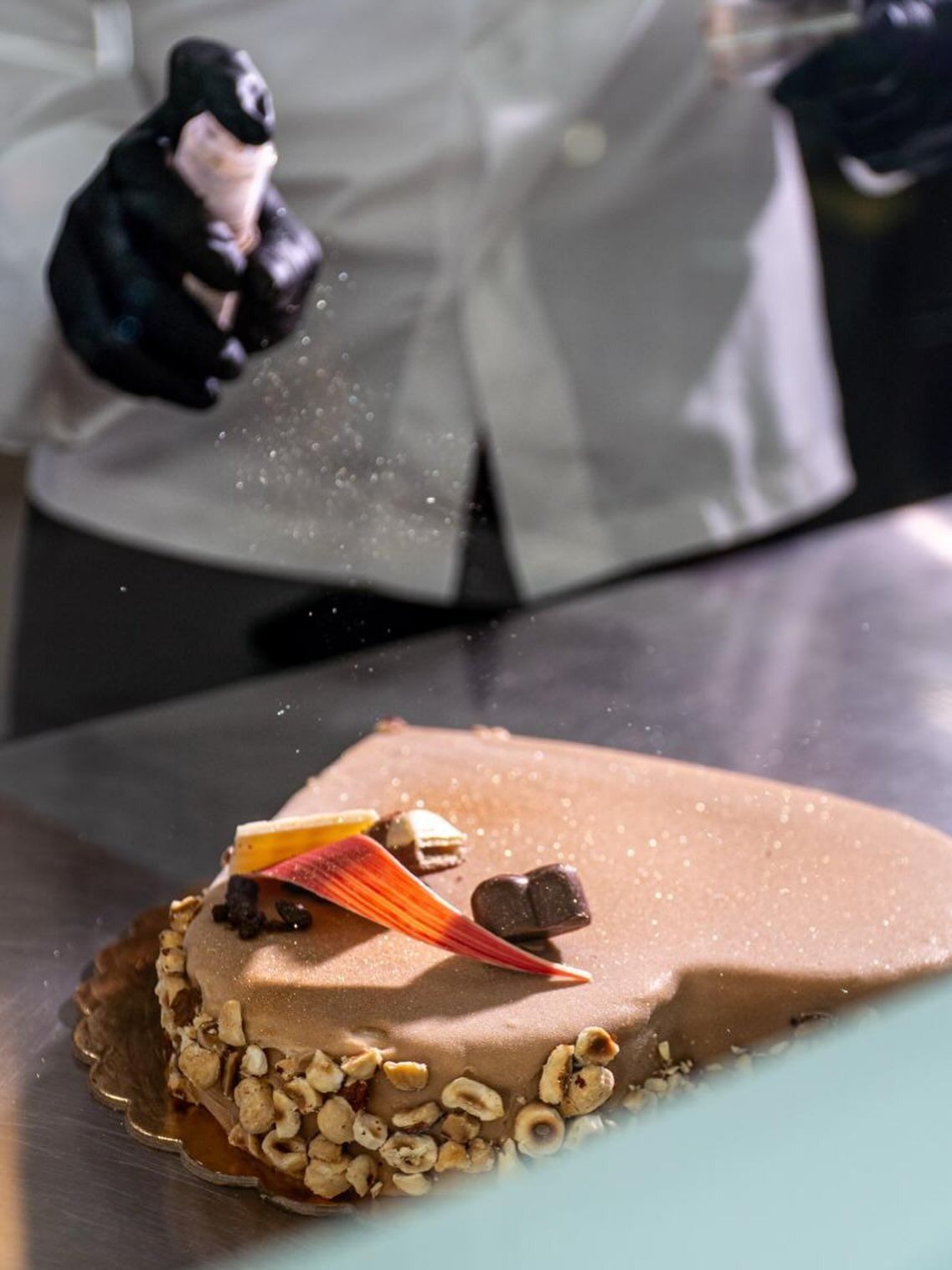 Fetta di torta di nocciole a strati con cioccolato, gelato, noci e un cucchiaio d'oro.