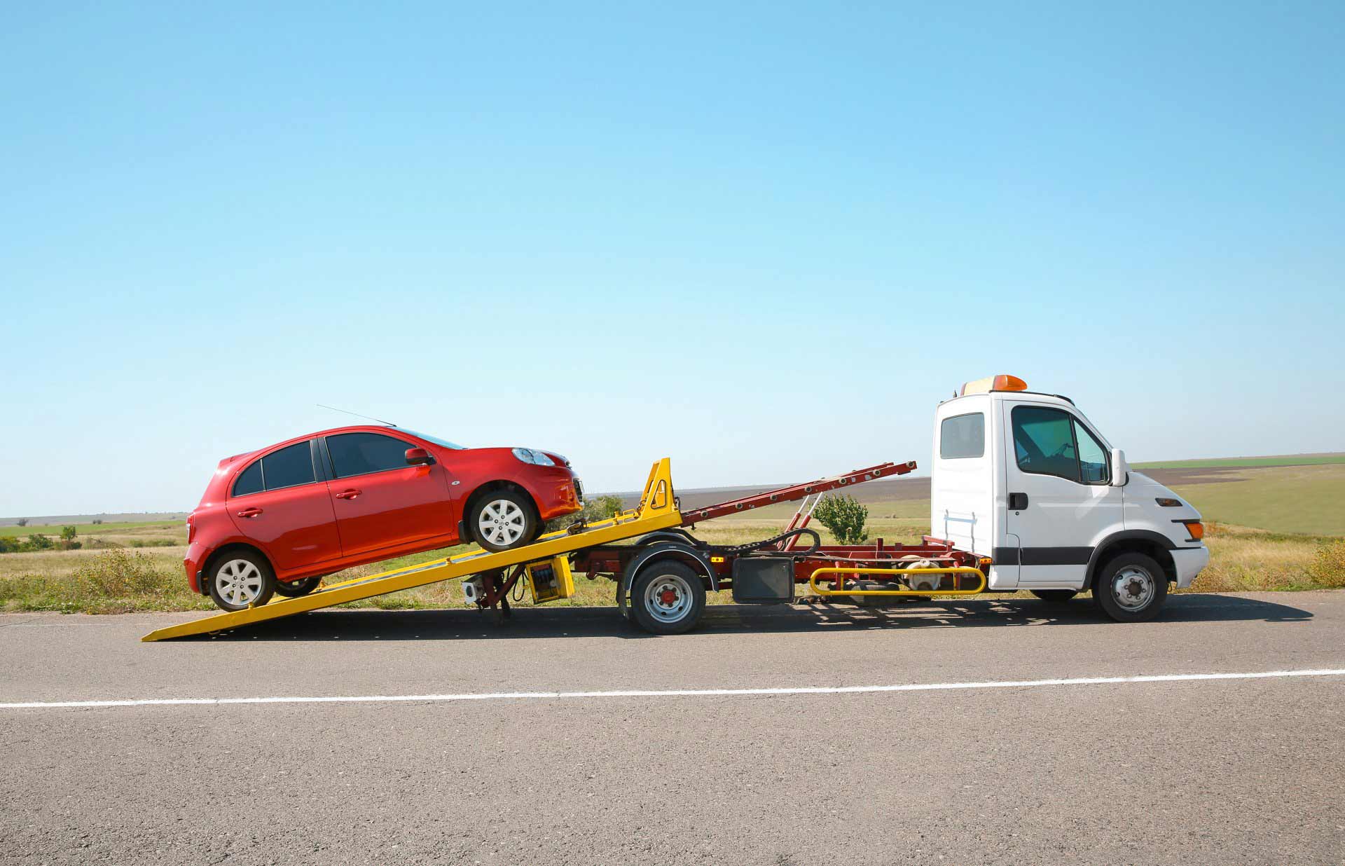 A Red Car is Being Towed by a Tow Truck on the Side of the Road — Murwillumbah Motor Wreckers in South Murwillumbah, NSW