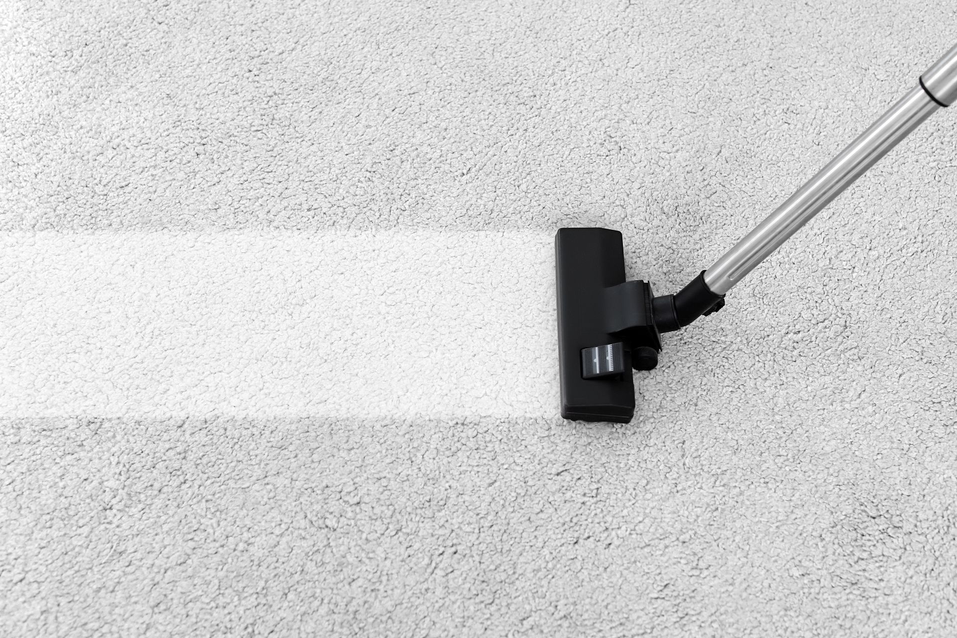 Vacuum cleaner cleaning a light gray carpet, leaving a clean white strip.