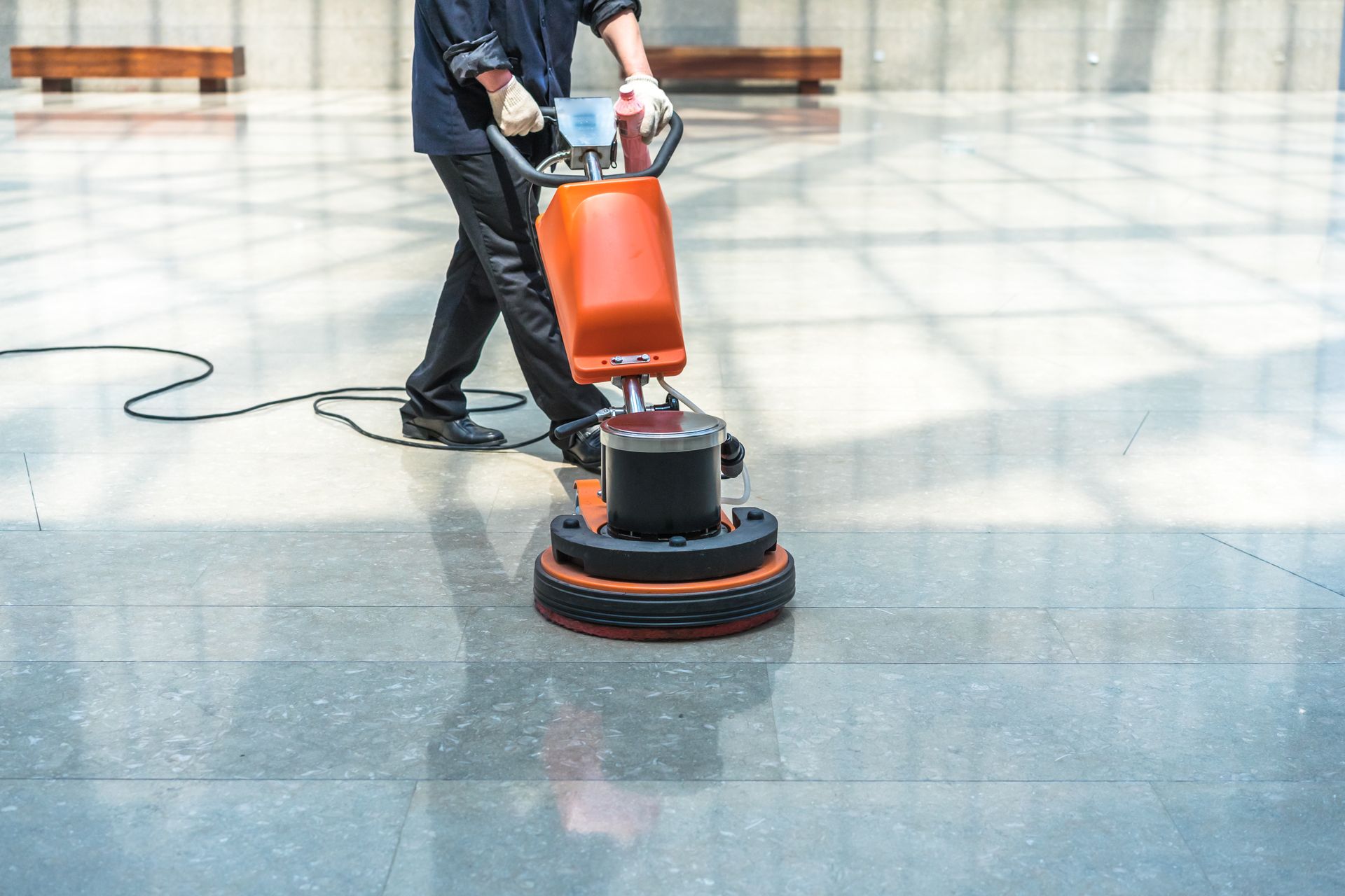 Person wearing orange gloves scrubbing a tiled floor with a brush.