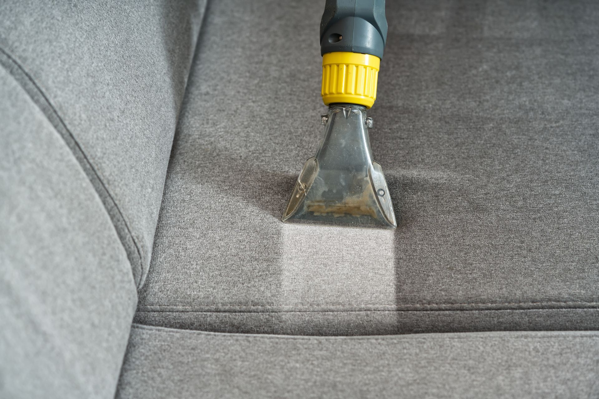 Upholstery cleaner nozzle cleaning a gray fabric sofa.