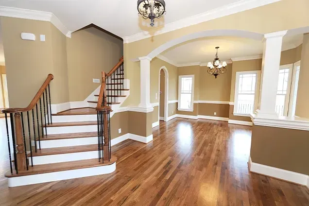 Empty interior with hardwood floors, staircase, and chandelier lighting. Beige walls with white trim.
