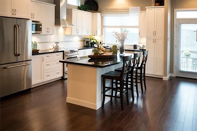 Modern kitchen with white cabinets, dark island, stainless steel appliances, and dark wood floors.