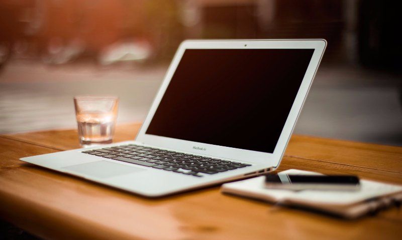 A laptop computer is sitting on a wooden table next to a glass of water.