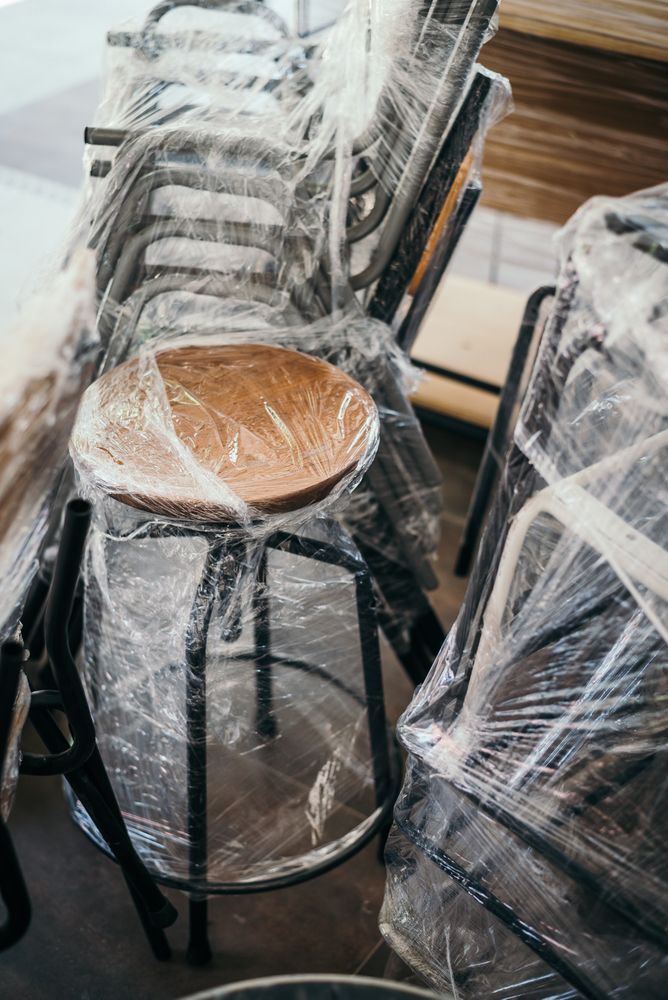 Chairs Wrapped in Clear Plastic, Stacked in A Warehouse or Storage Area — Westlake Removals in Morisset, NSW