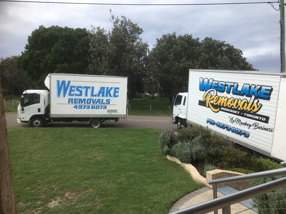 Two White Westlake Removal Trucks Parked on A Grassy Area Near a Road with Trees — Westlake Removals in Mannering Park, NSW