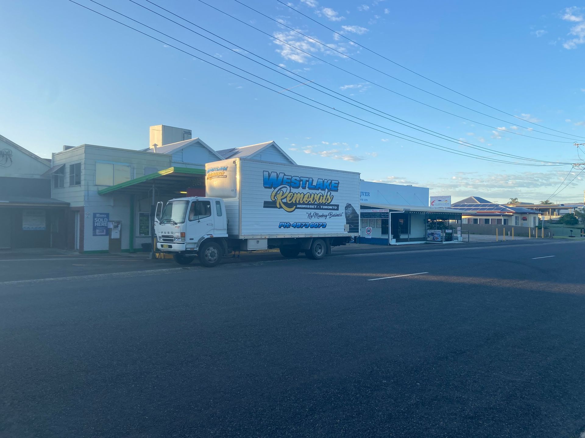 A white box truck parked in front of a building with a blue awning on a street.