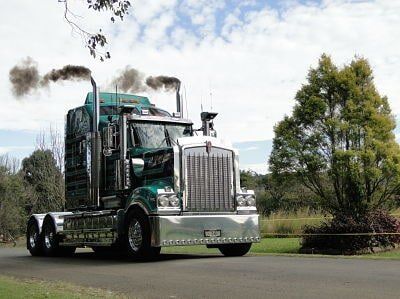 A Green Semi Truck Is Driving Down A Road Next To Trees — Clarence Valley Tyre Centre in South Grafton, NSW