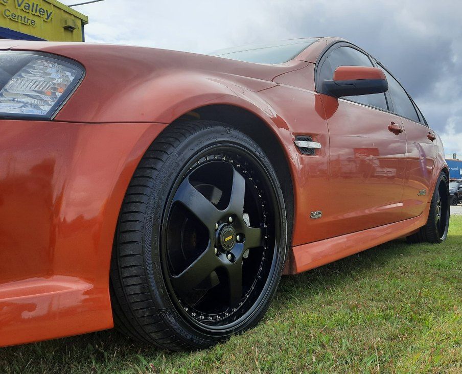 An Orange Car With Black Wheels Is Parked In The Grass — Clarence Valley Tyre Centre in South Grafton, NSW