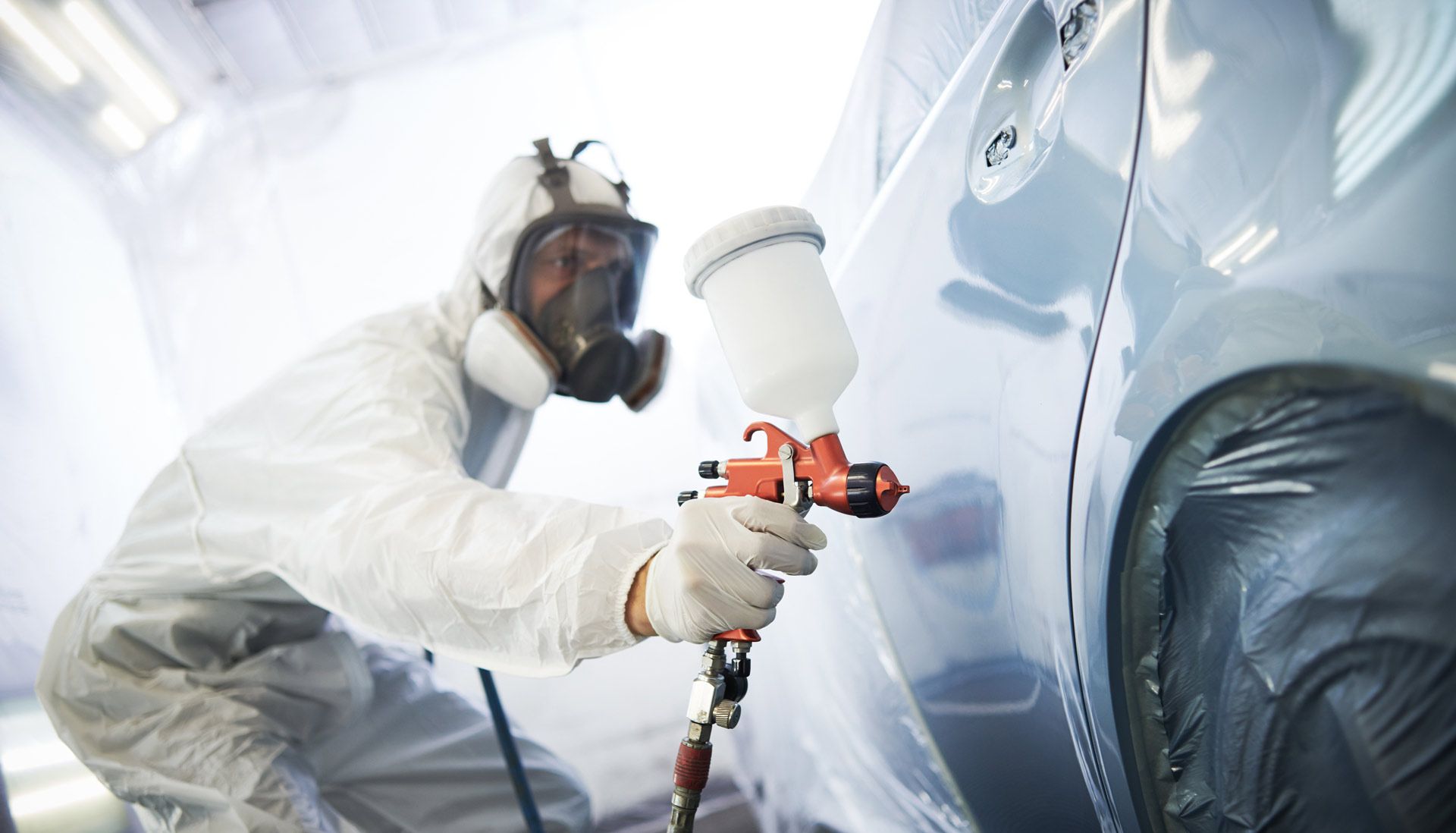 A man is painting a car in a paint booth.