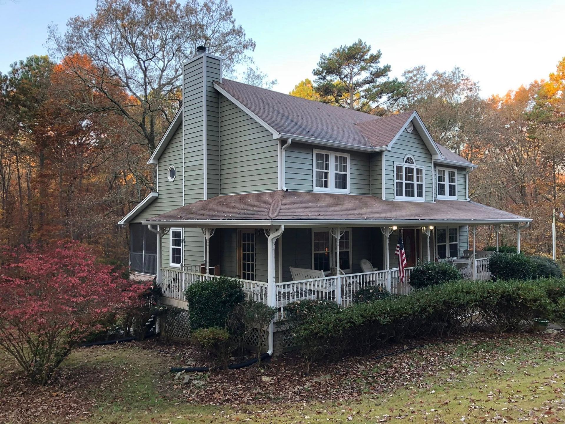 A large house with a porch in the middle of a forest.