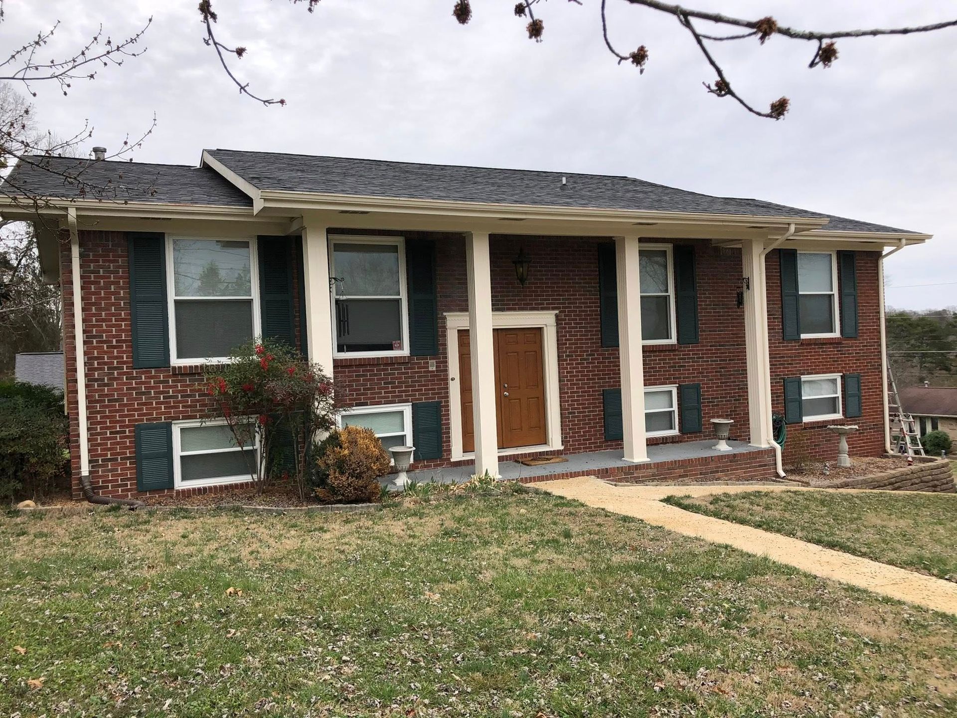A brick house with a porch and shutters on the windows.