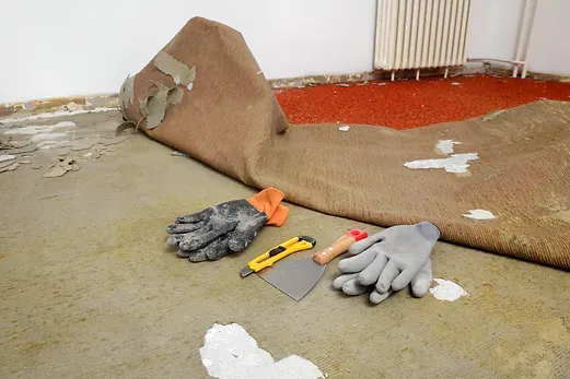 A piece of carpet is laying on the floor next to a pair of gloves and a spatula.
