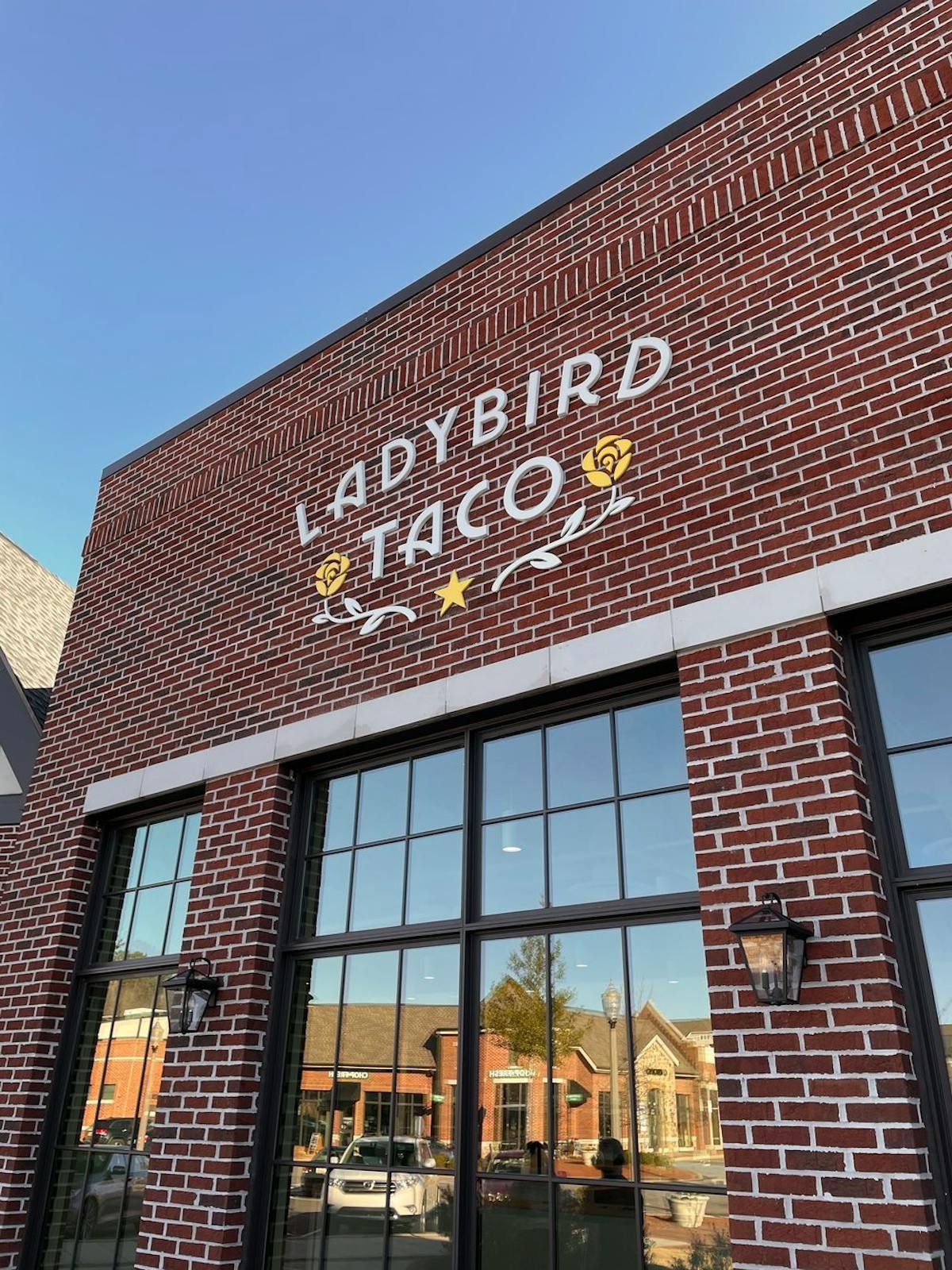 Exterior view of a brick building with a sign reading "LADYBIRD TACO" and large windows under a clear blue sky.