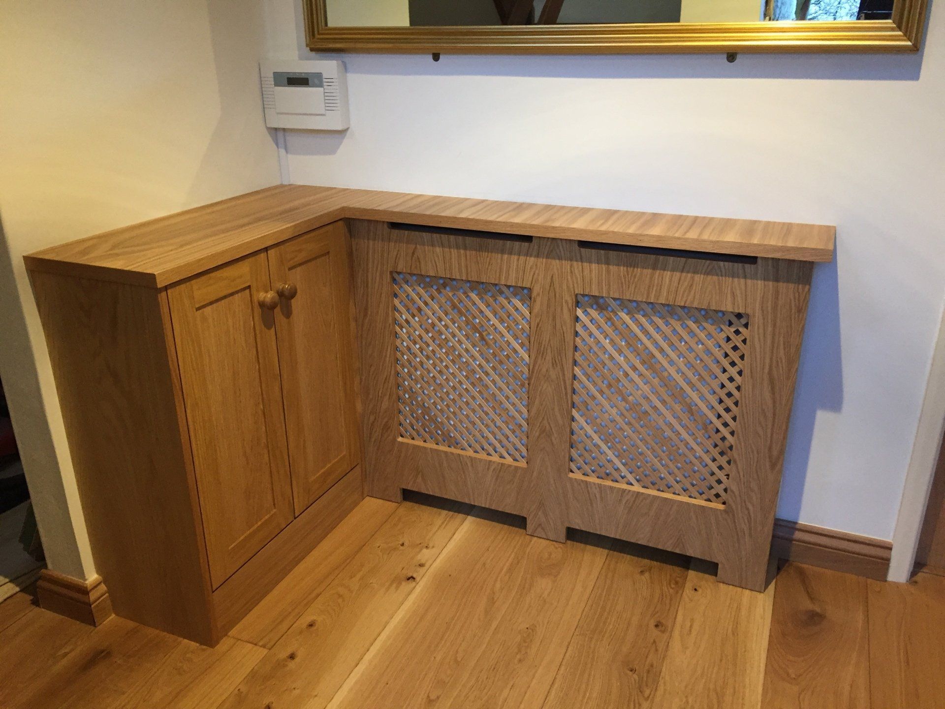 A wooden cabinet with a radiator cover and a mirror in a hallway.
